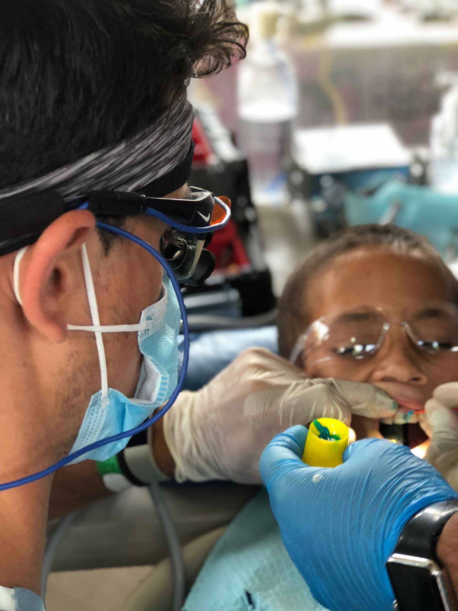 A man wearing a mask and gloves is working on a child 's teeth