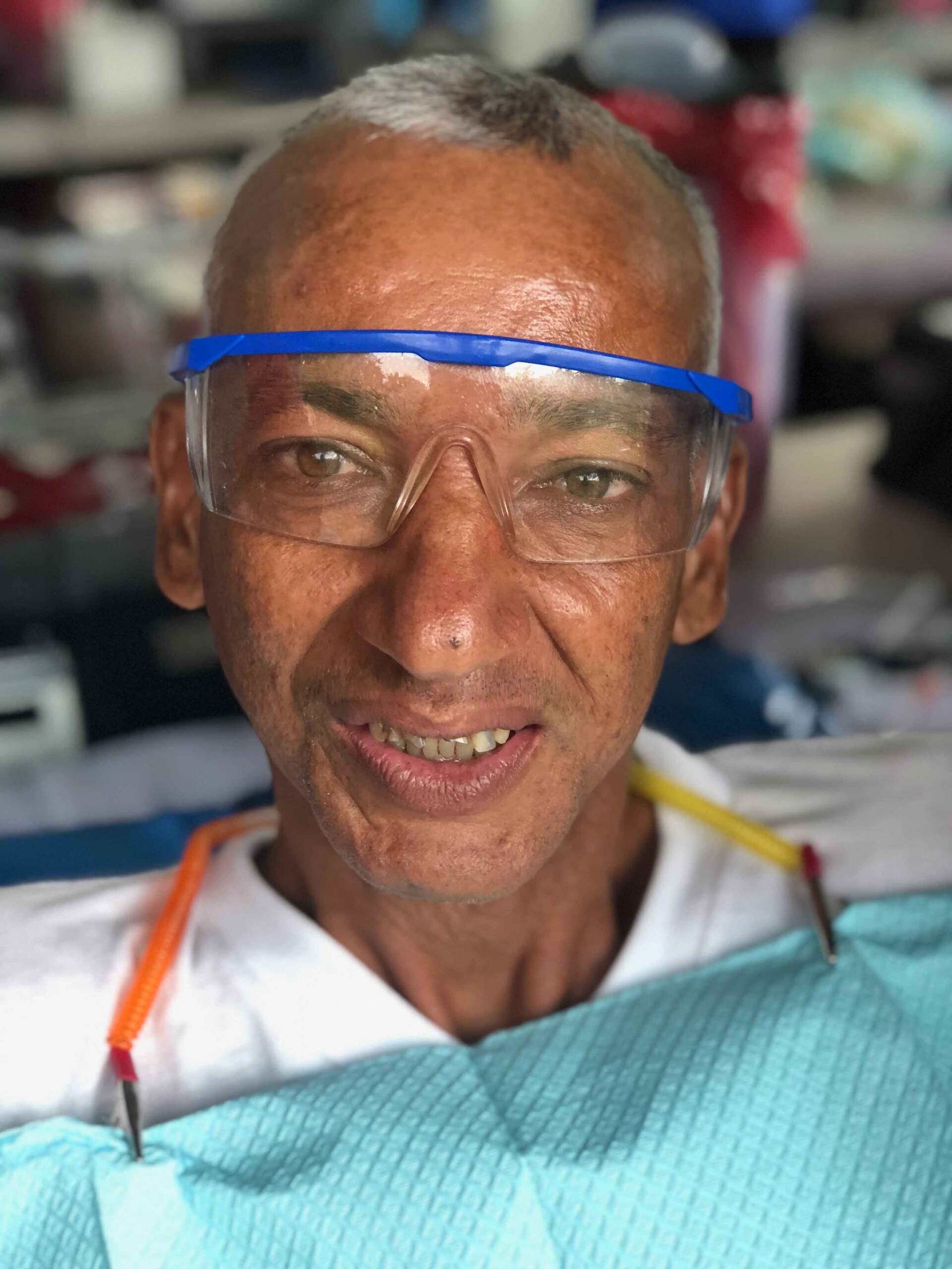 A man wearing glasses and braces is smiling in a dental chair.