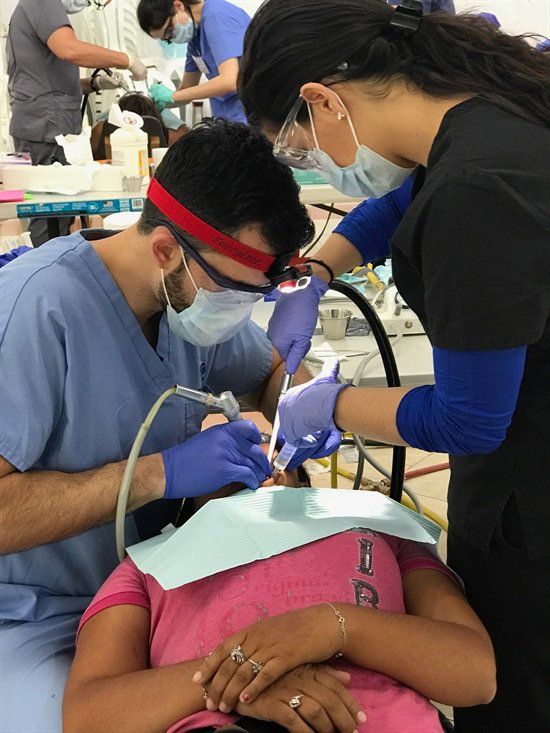 A girl in a pink shirt is getting her teeth examined by two dentists