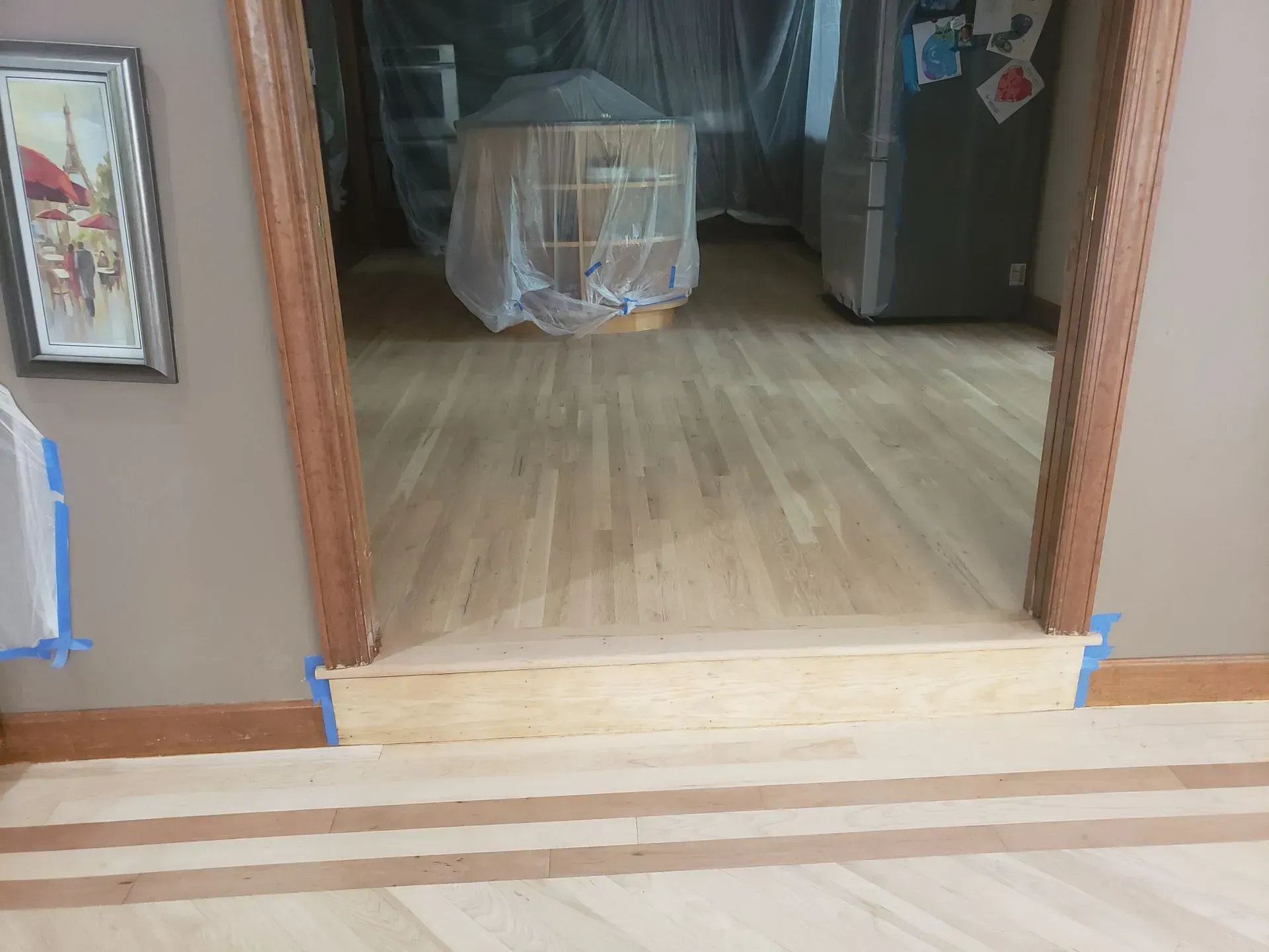Wood floors and doorway with a small step; masking tape on the edges.