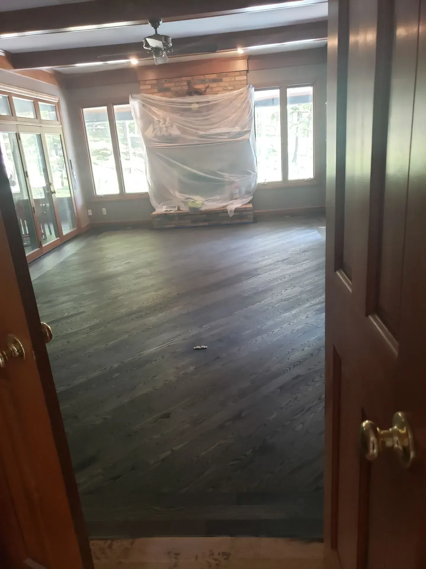 Dark stained hardwood floor in a sunroom with a fireplace covered in plastic and large windows.