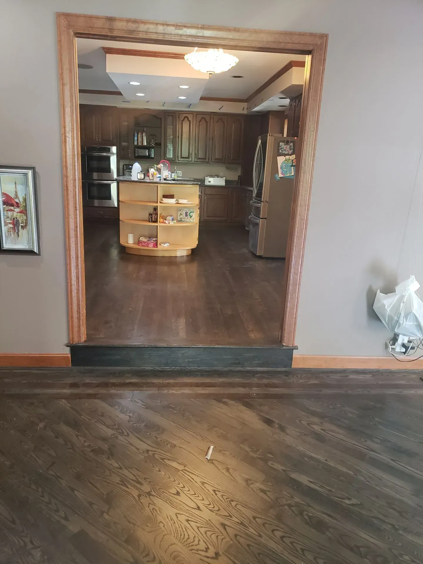 Wooden doorway leading into a kitchen with dark hardwood floors, cabinets, and island.