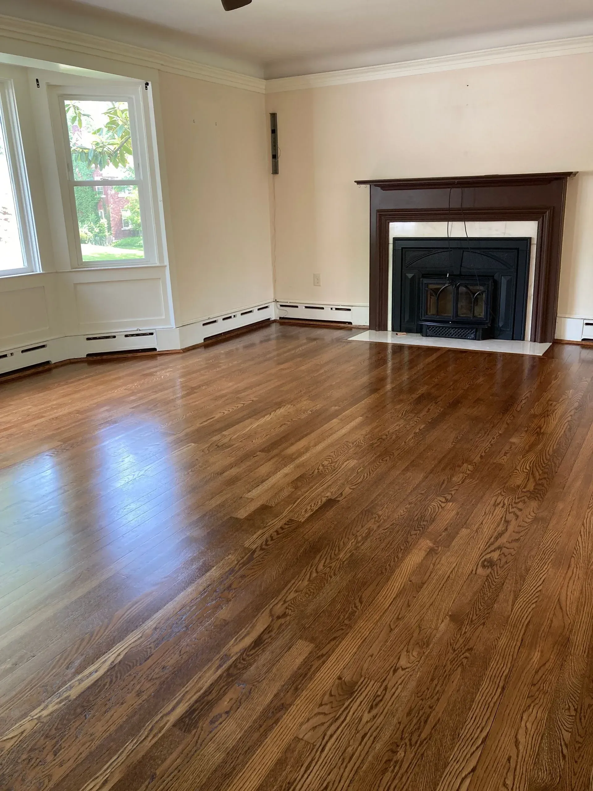 Empty room with hardwood floors, fireplace, and window; beige walls and white trim.