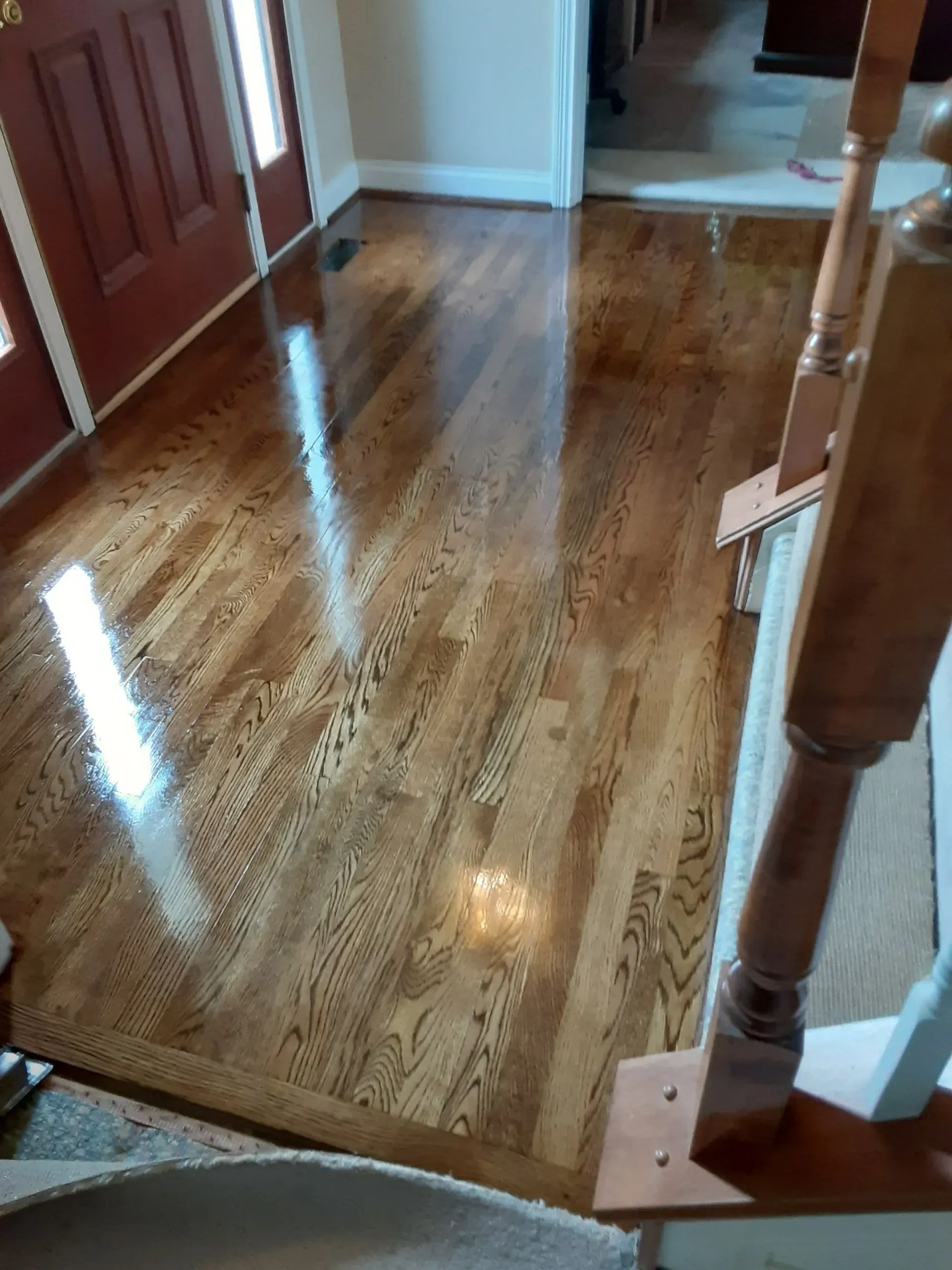Hardwood floor with glossy finish in an entryway, with reddish-brown door and wooden stair banister.
