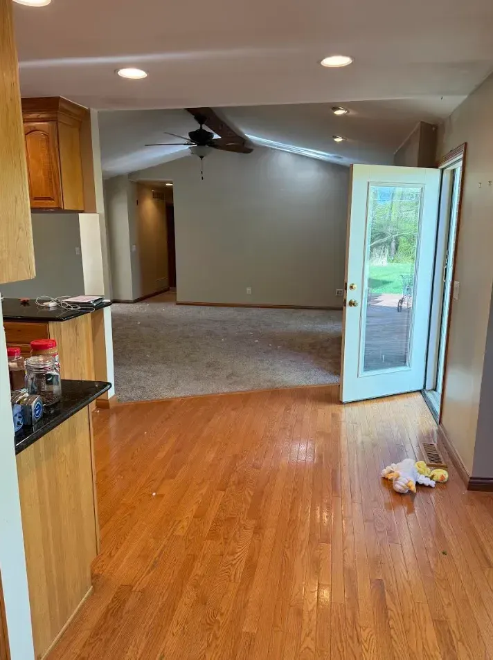 Kitchen with wood floors, open to a living area with carpet. A glass door leads outside.