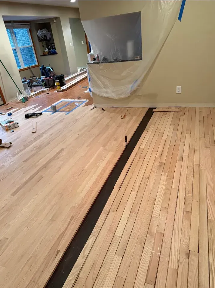 Hardwood floor installation in progress; wood planks laid out with a dark strip between sections.
