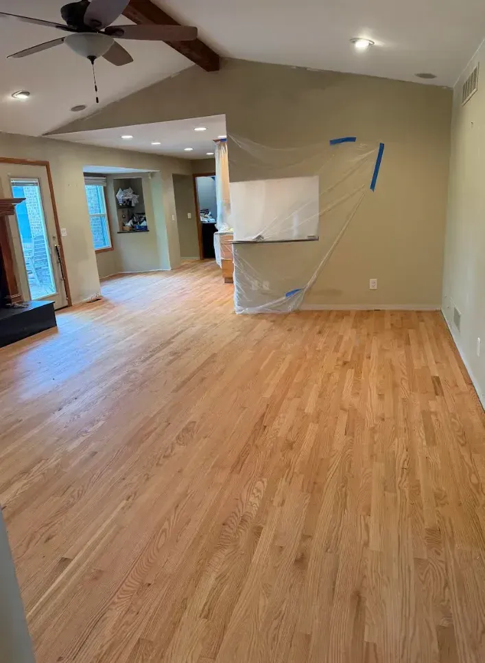 Newly installed hardwood floors in a home. The room is mostly empty with beige walls and a white board covered in plastic.