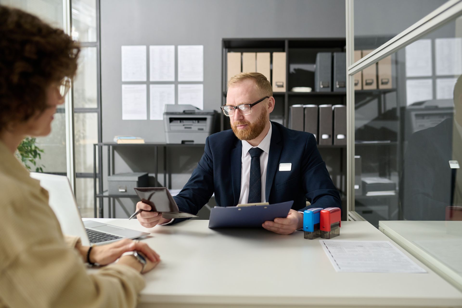A man in a suit and tie is sitting at a desk talking to a woman.