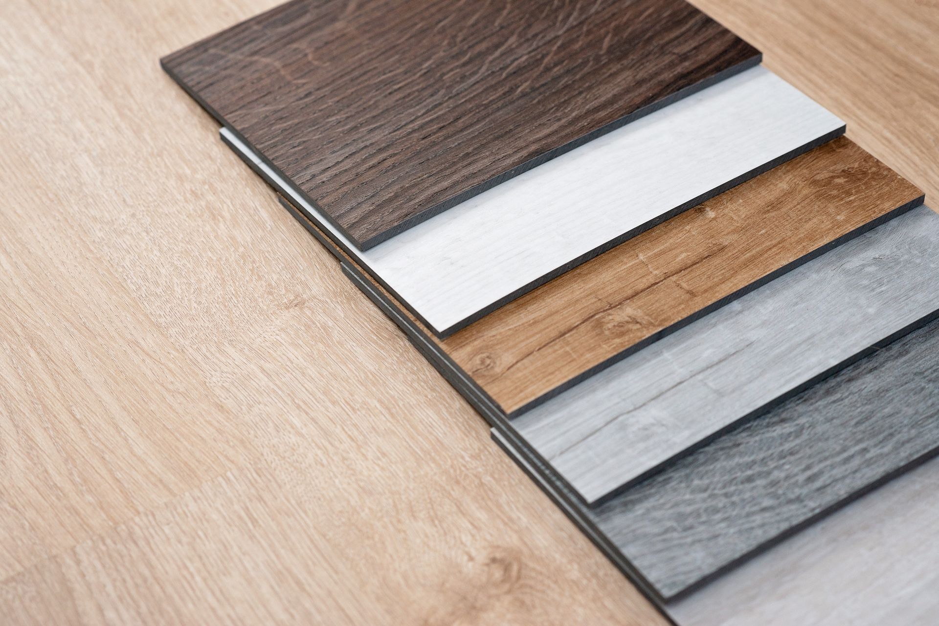 Floorboard samples in various wood tones stacked on a light wood floor.