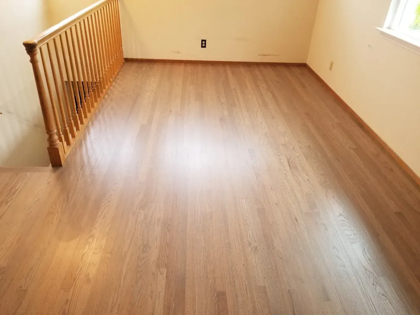Hardwood floor with wooden railing. Beige walls. Room is empty.