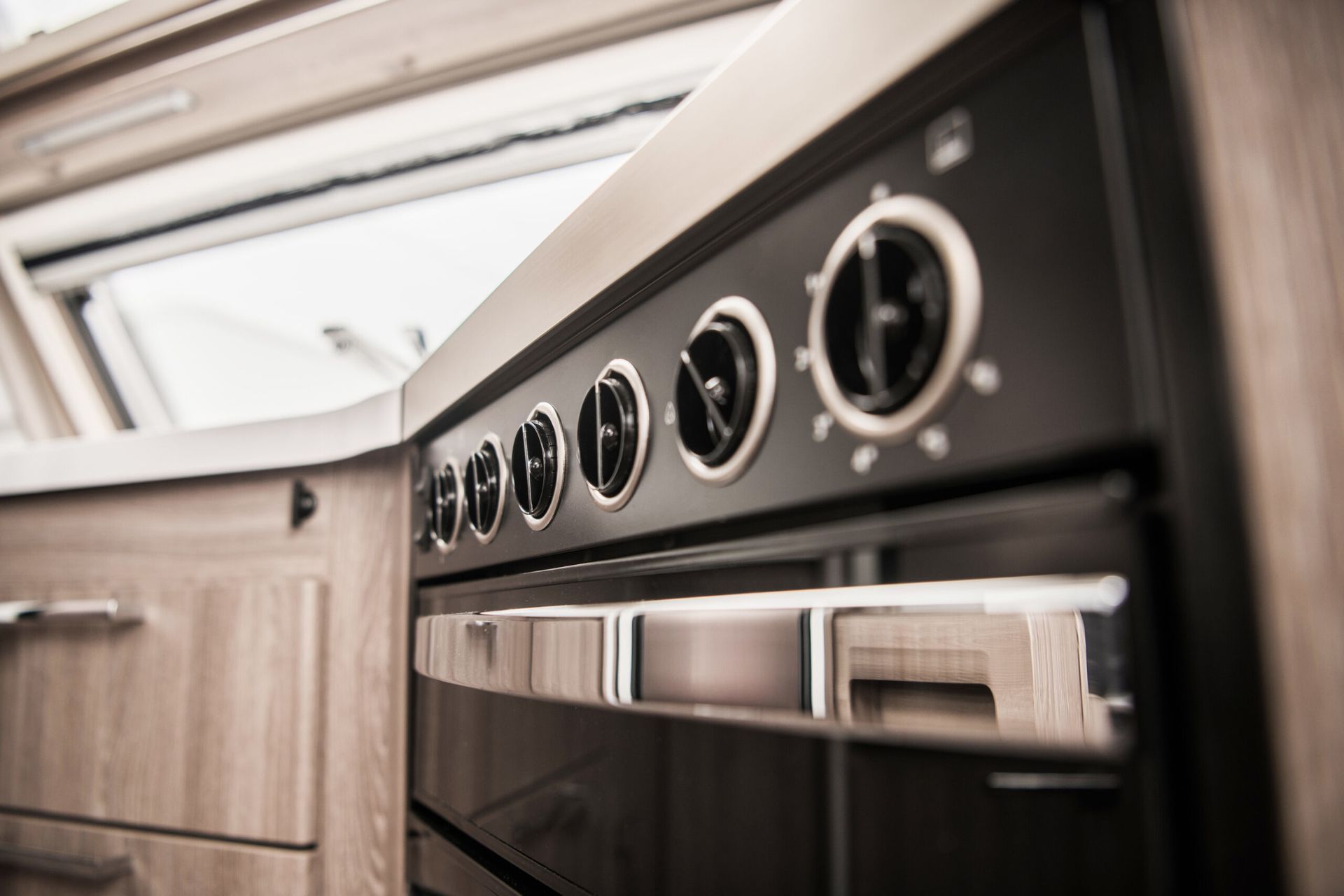 Close-up of a black and silver oven with control knobs and a glass door, inside a wooden-paneled RV kitchen.