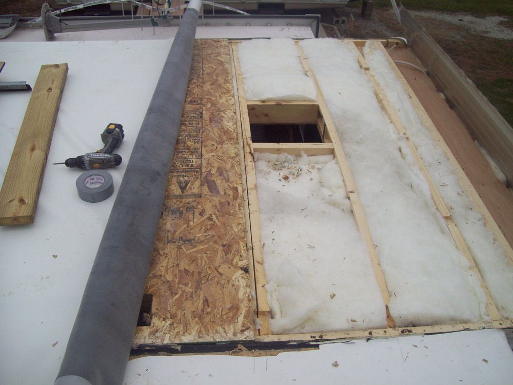 Rooftop repair in progress. Wood frame with insulation exposed. Grey roll of material and tools nearby.