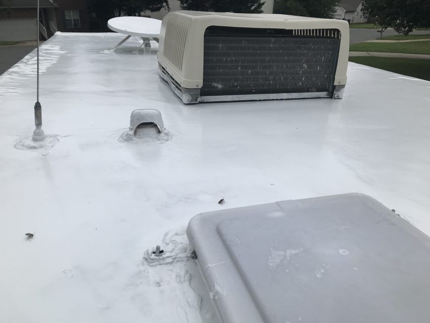 White RV roof with air conditioner, antenna, and satellite dish. The roof is painted with a white sealant.