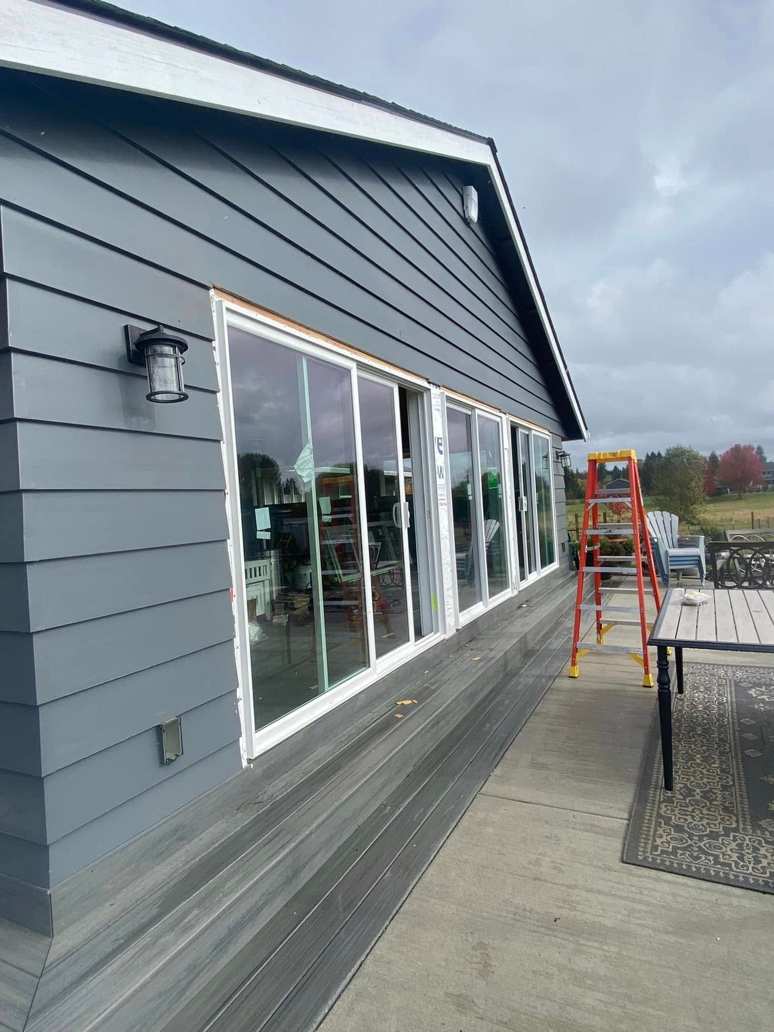 Gray storefront with large windows, a ladder on the sidewalk, and an overcast sky.