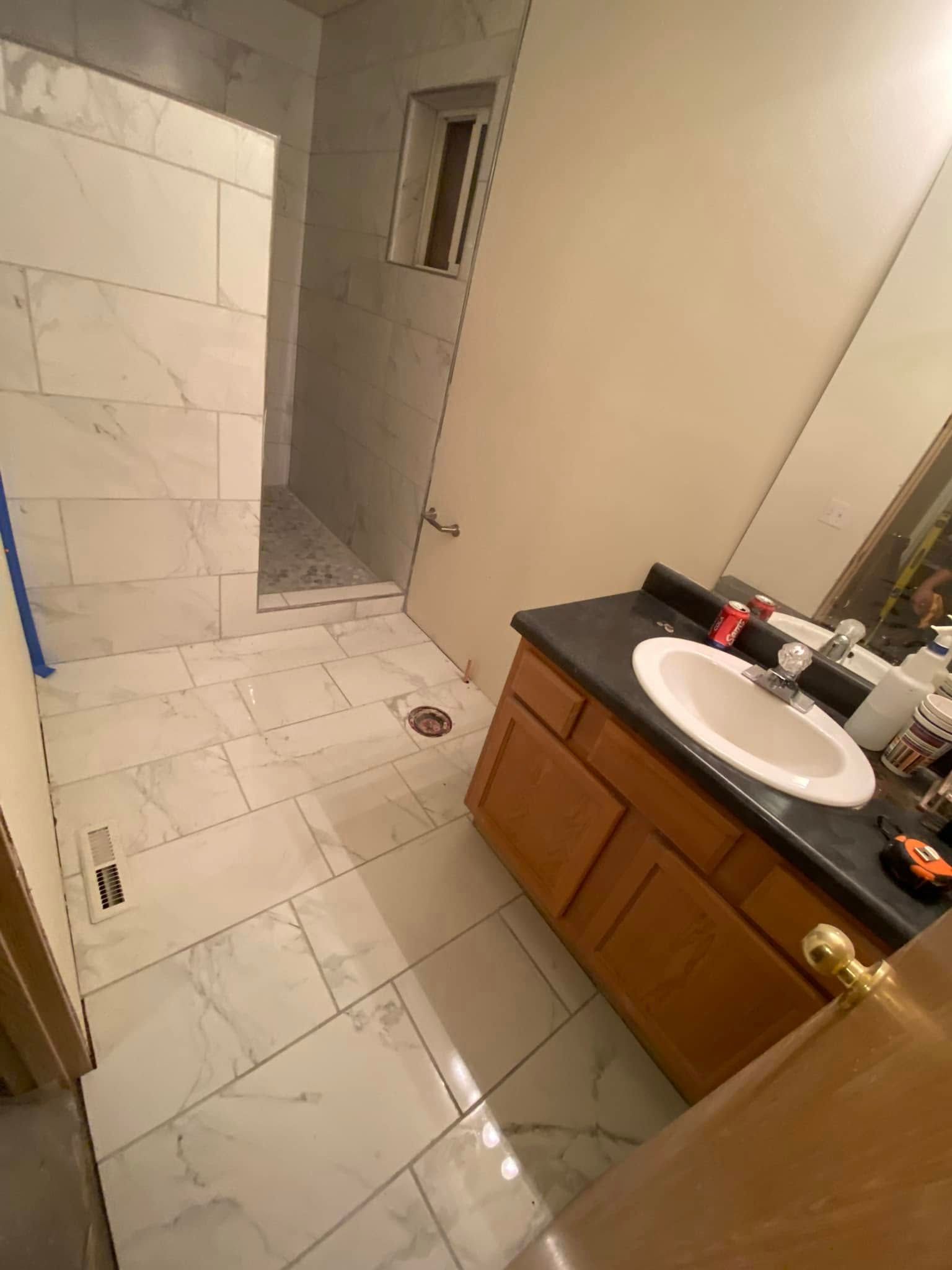 Bathroom with white tile, wood vanity, black countertop, and a doorway to a tiled shower.