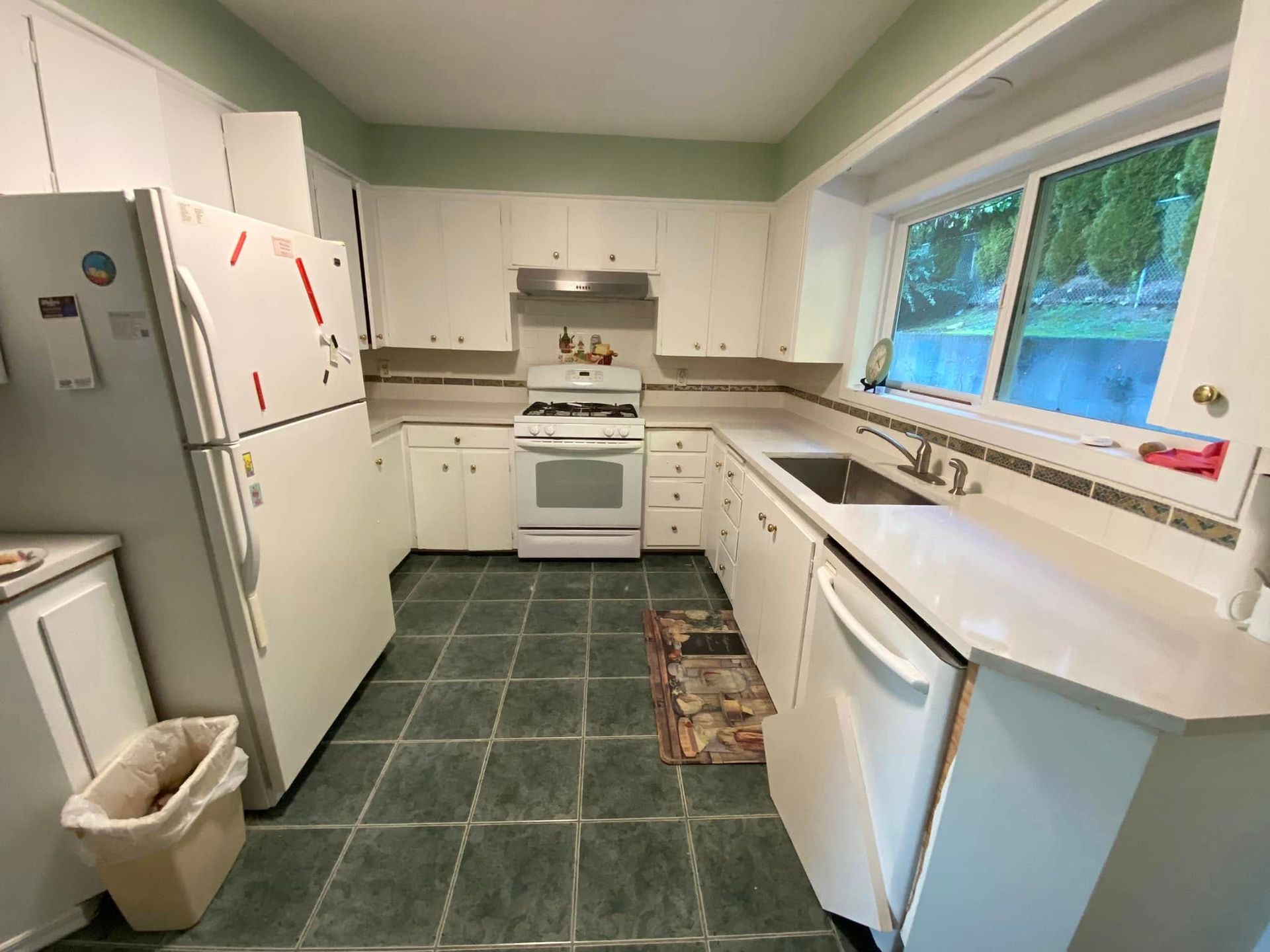 Small white kitchen with green tile floor, refrigerator, stove, sink, and window over the counter.