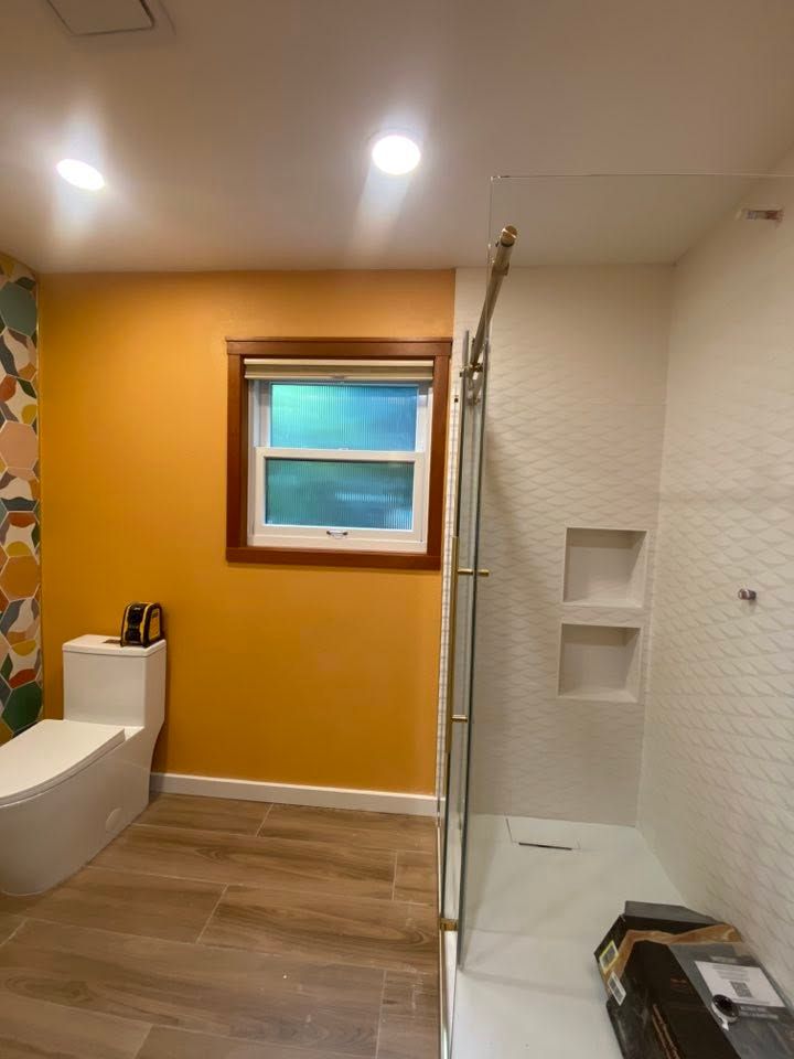 Bathroom with orange wall, window, walk-in shower, and toilet under recessed lights
