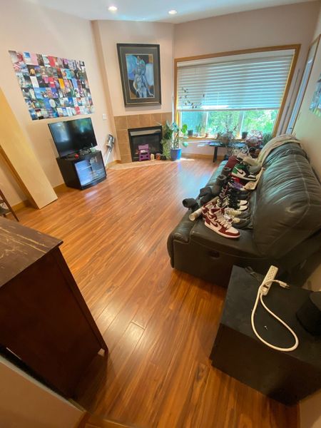 Bright living room with wood floor, black leather sofa, window blinds, fireplace, and colorful wall art