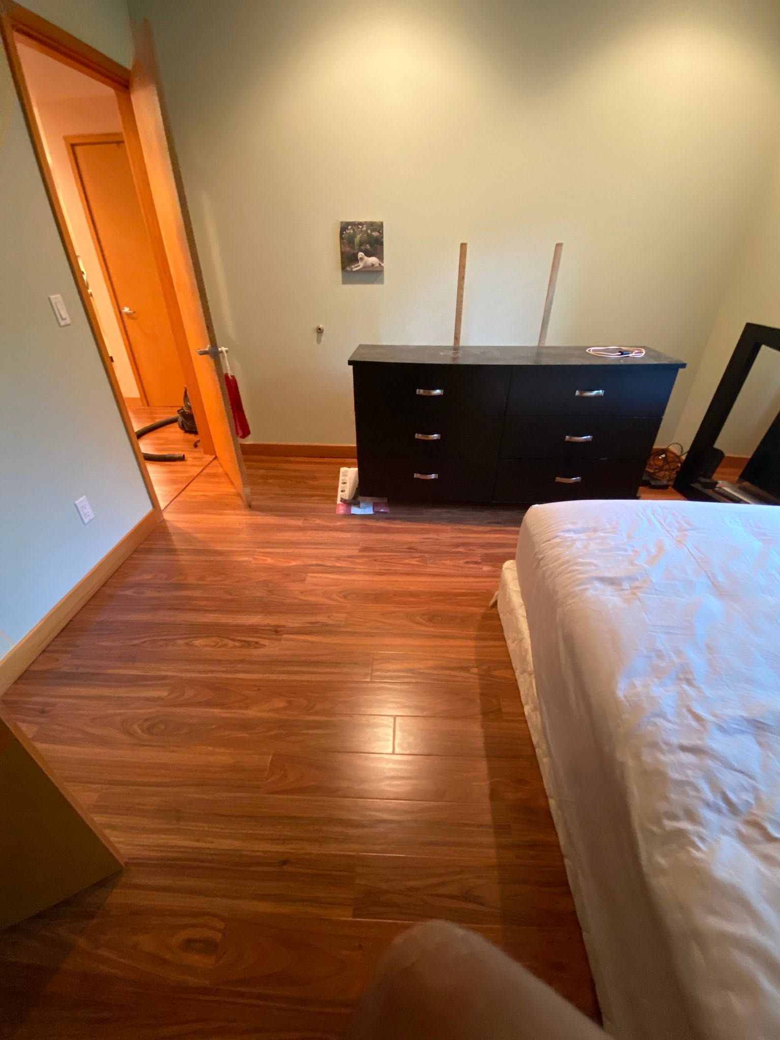 Bedroom with bed, dark dresser, and open door on a hardwood floor.
