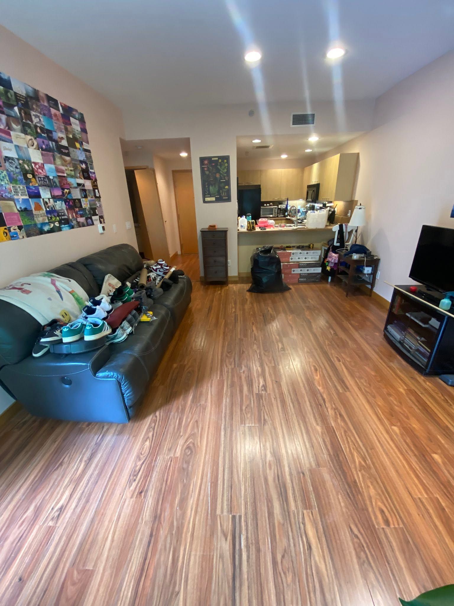 Living room with a black sofa, colorful wall art, wood floors, and an open kitchen in the background