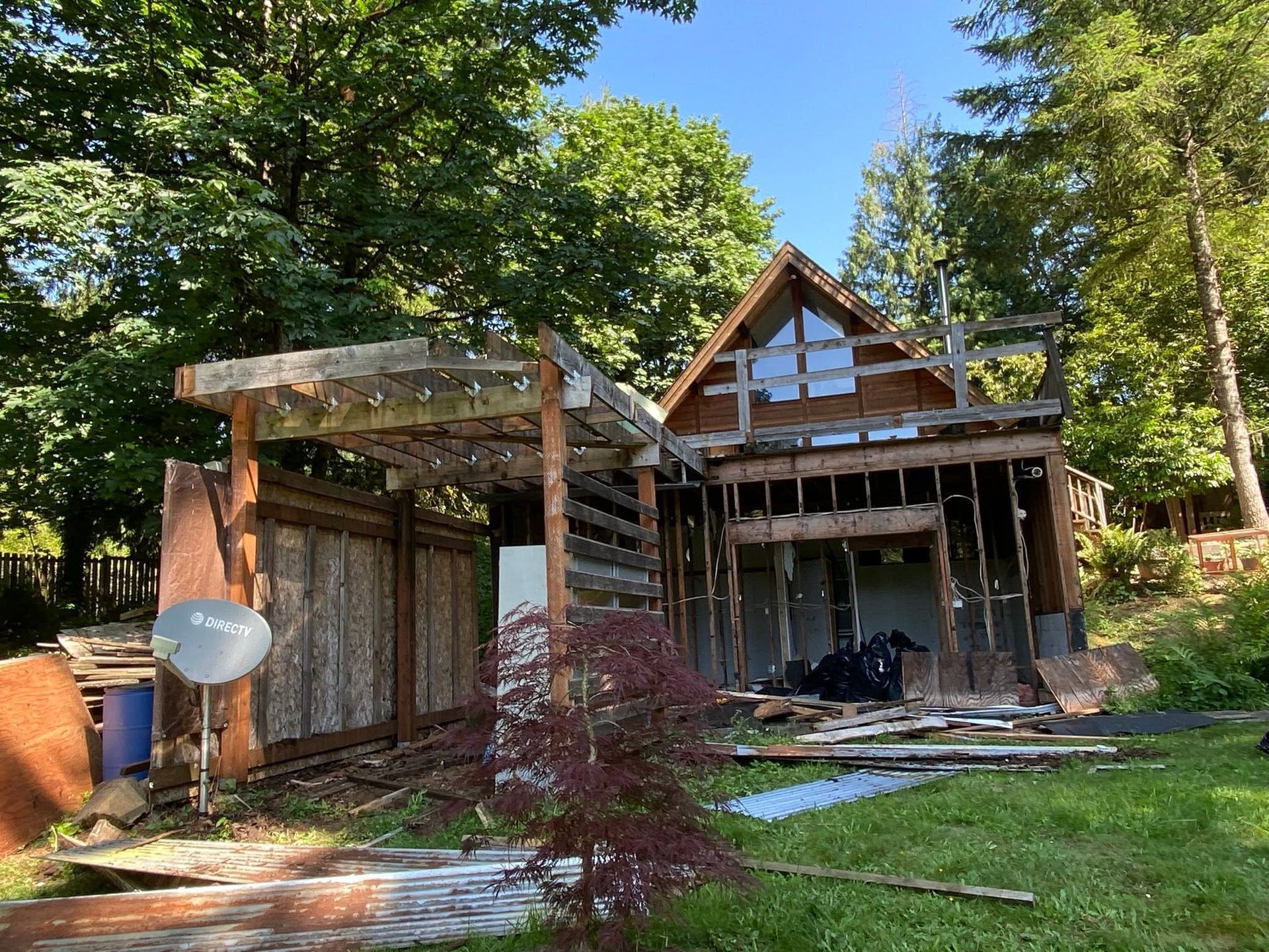 House under construction with wooden framing, scaffolding, and a covered porch in a wooded yard