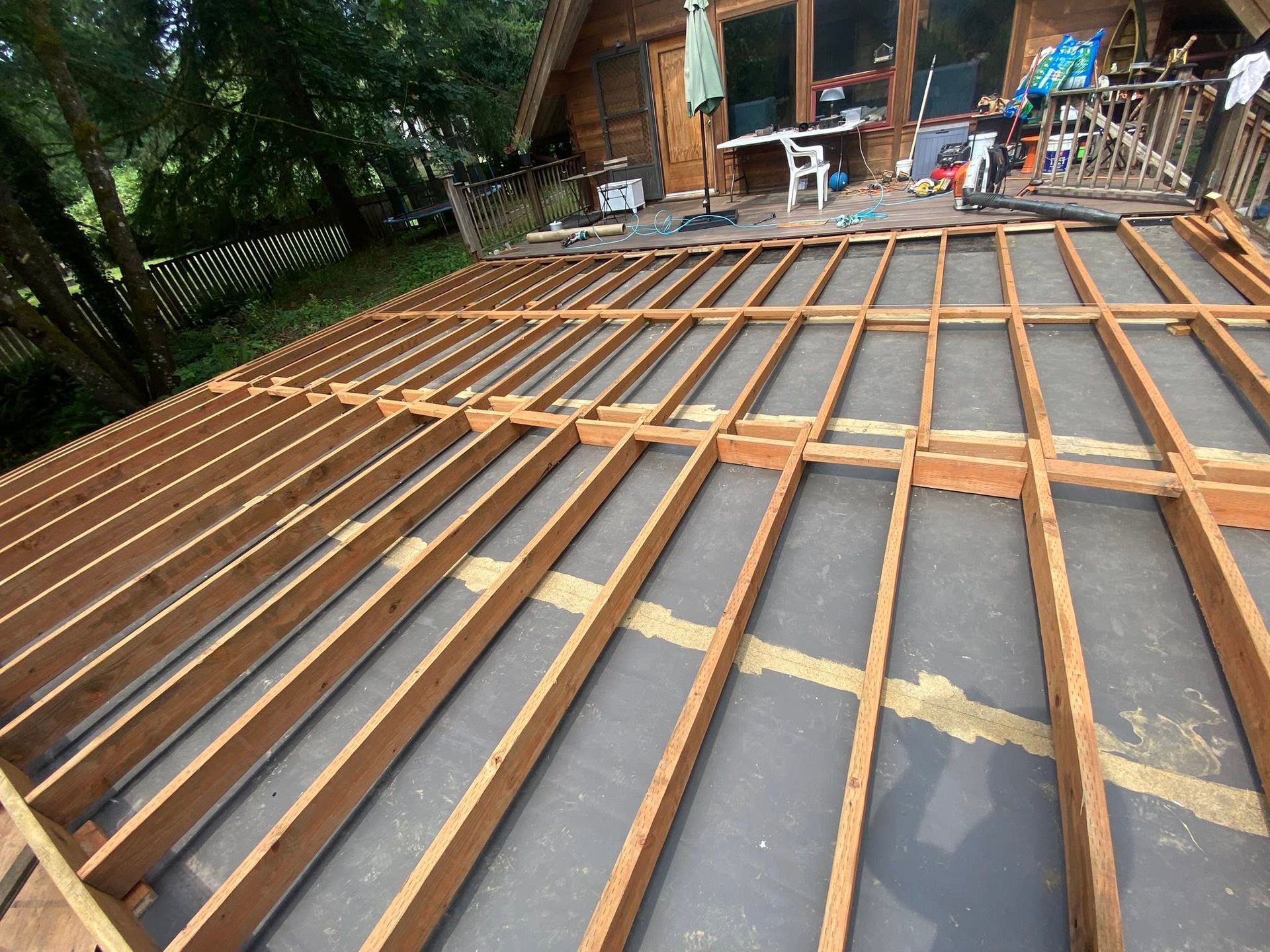 Wooden roof framing over black roofing felt beside a cabin under construction