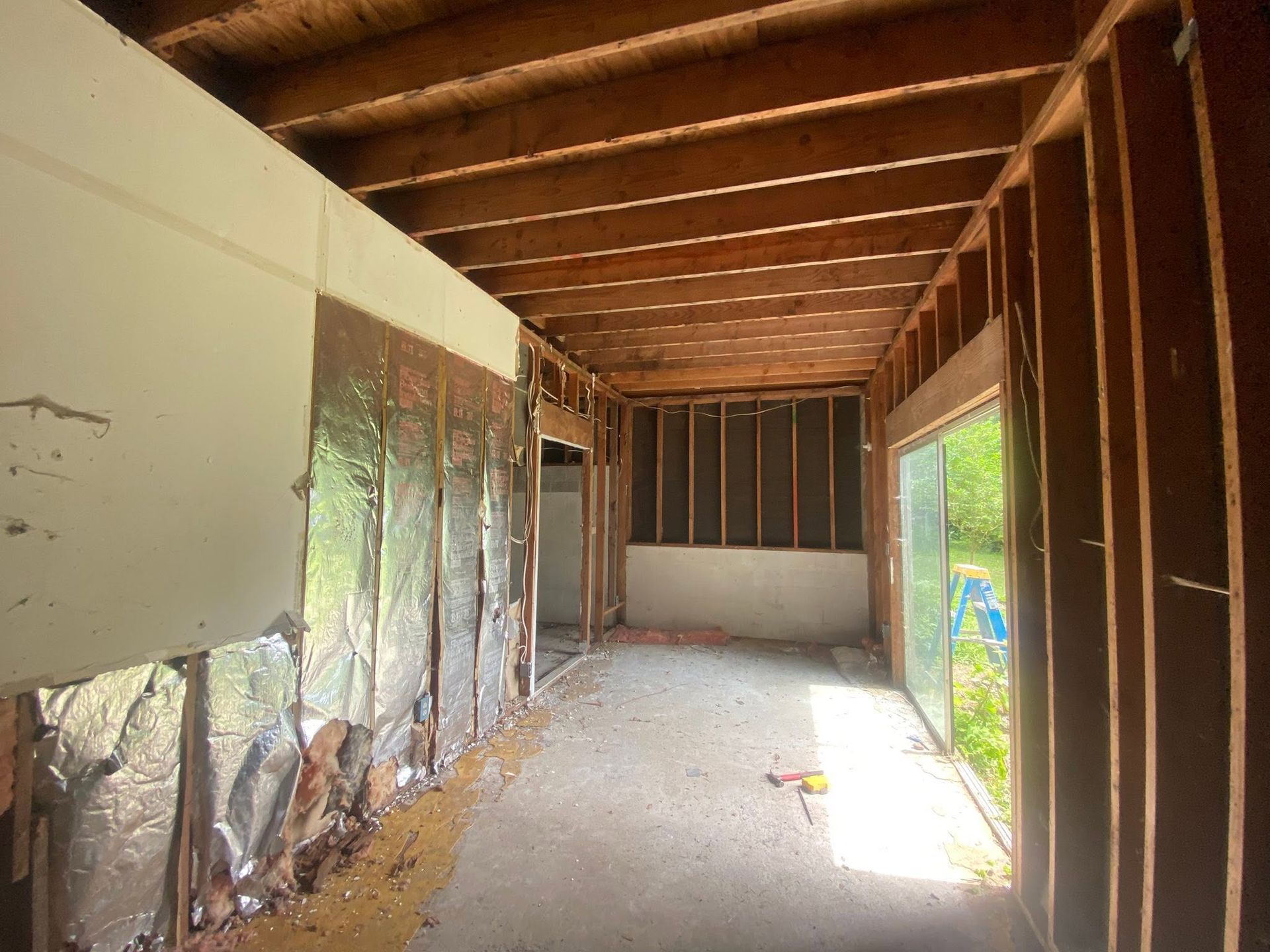 Partially demolished room with exposed wall studs, debris on the floor, and daylight through open side windows.