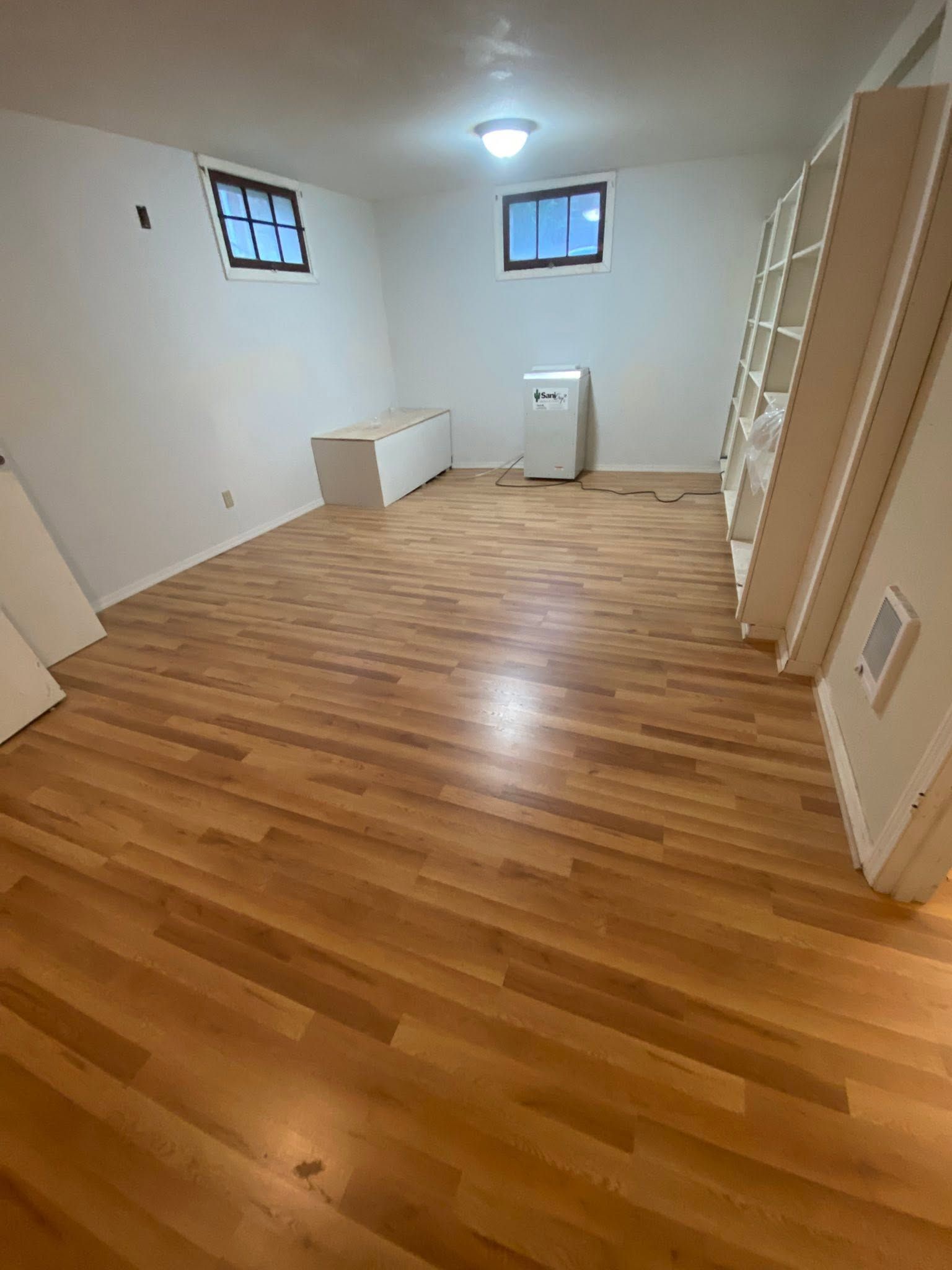 Empty room with hardwood floors, white walls, two windows, and built-in shelving along one side