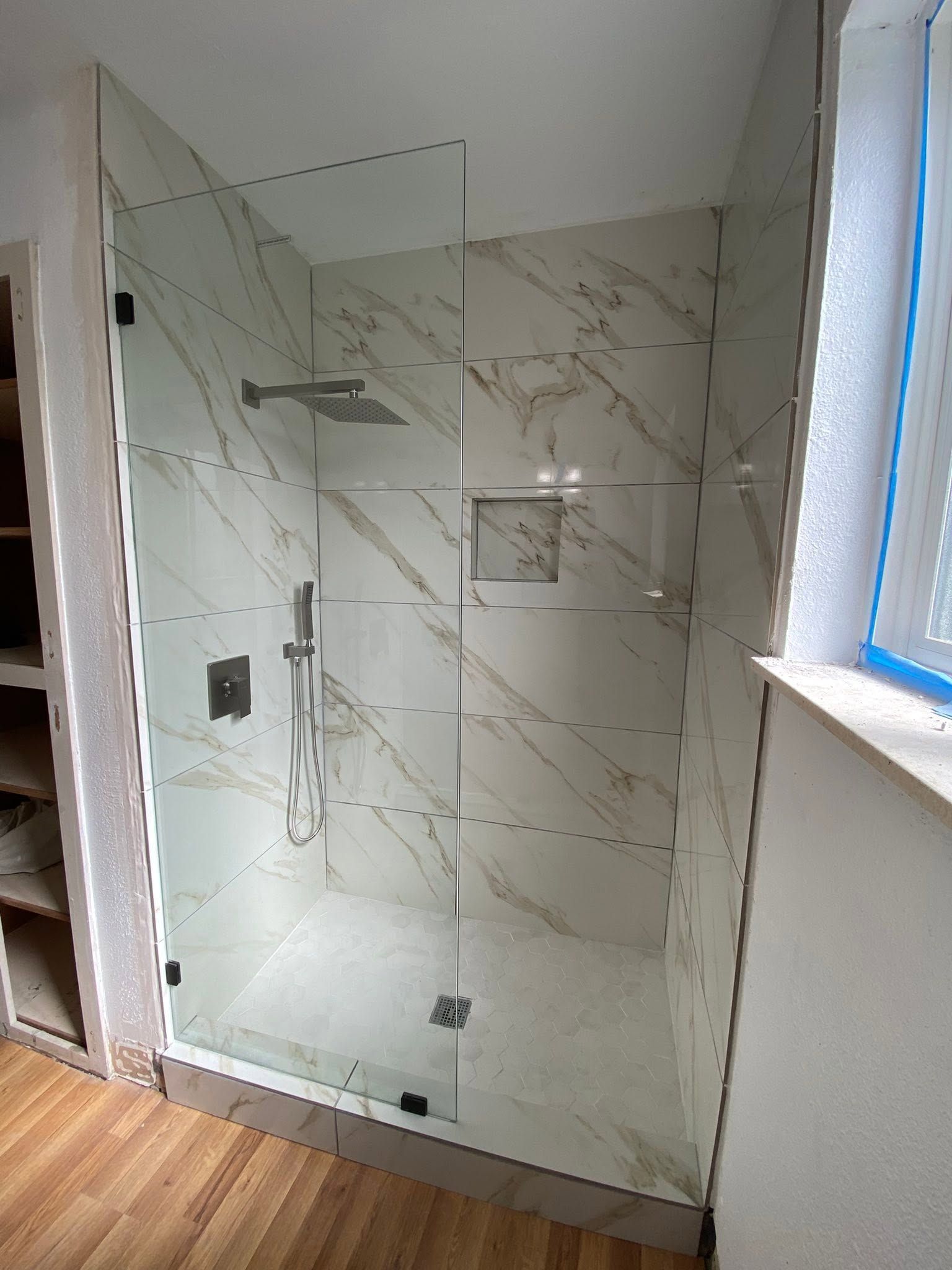 Modern marble-tiled walk-in shower with glass enclosure and rainfall showerhead in a bathroom