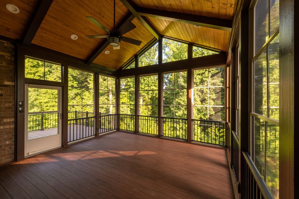 Empty sunroom with wood ceiling, brick floor, and large windows overlooking trees and a balcony