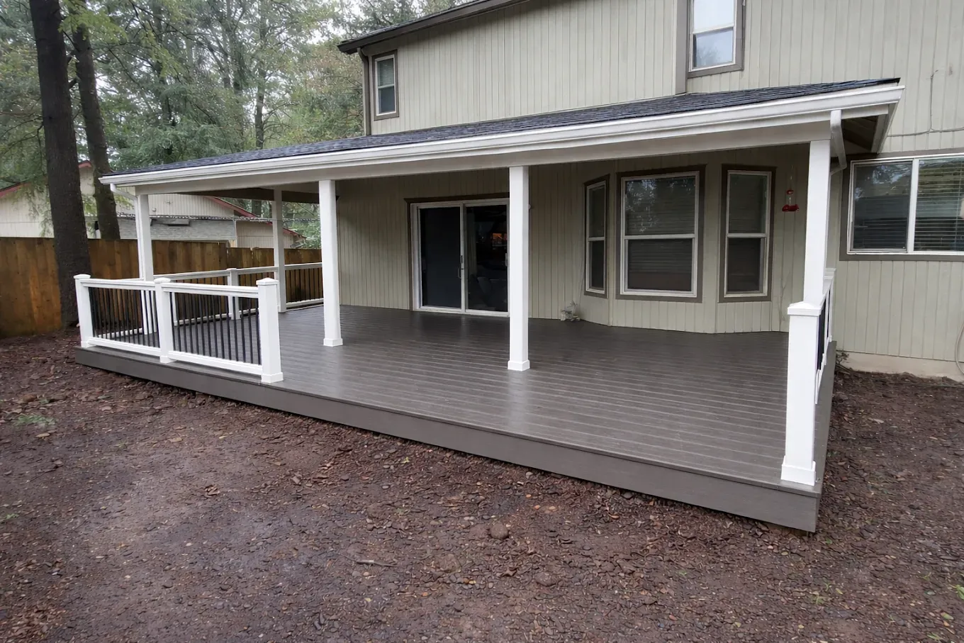 House with a covered wooden deck and white railings in a wooded yard