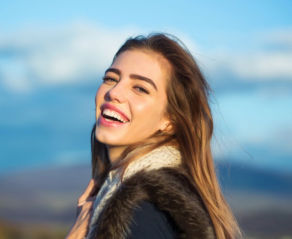 A woman wearing a fur coat and scarf is smiling.