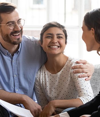 A woman is talking to a man and a woman while sitting at a table with a laptop.