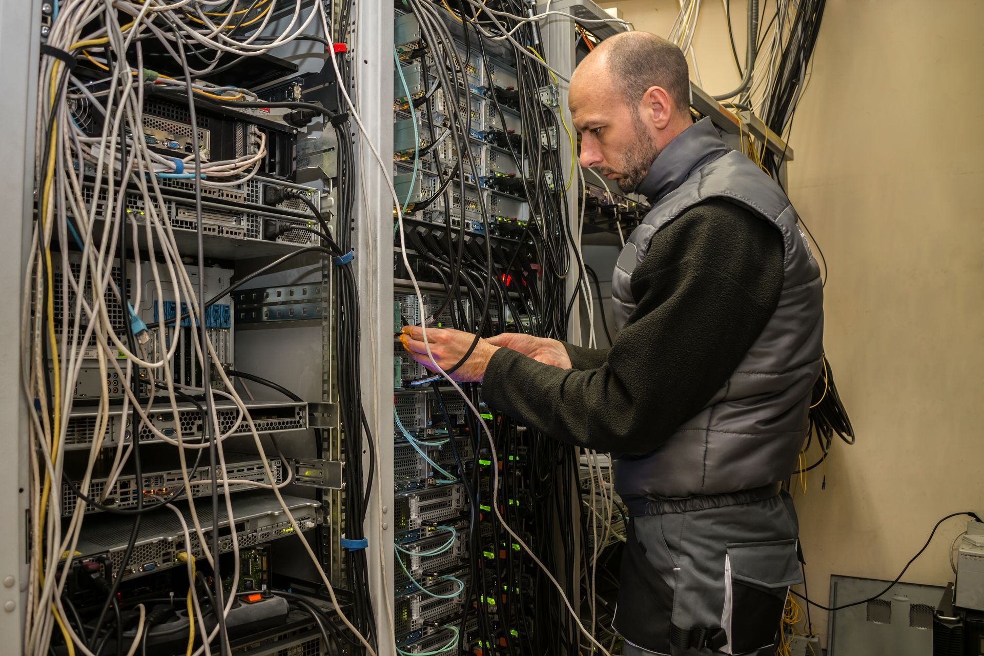 Man Working on A Server Rack Filled with Tangled Cables — SJD Electrical Contracting in Parkes, NSW