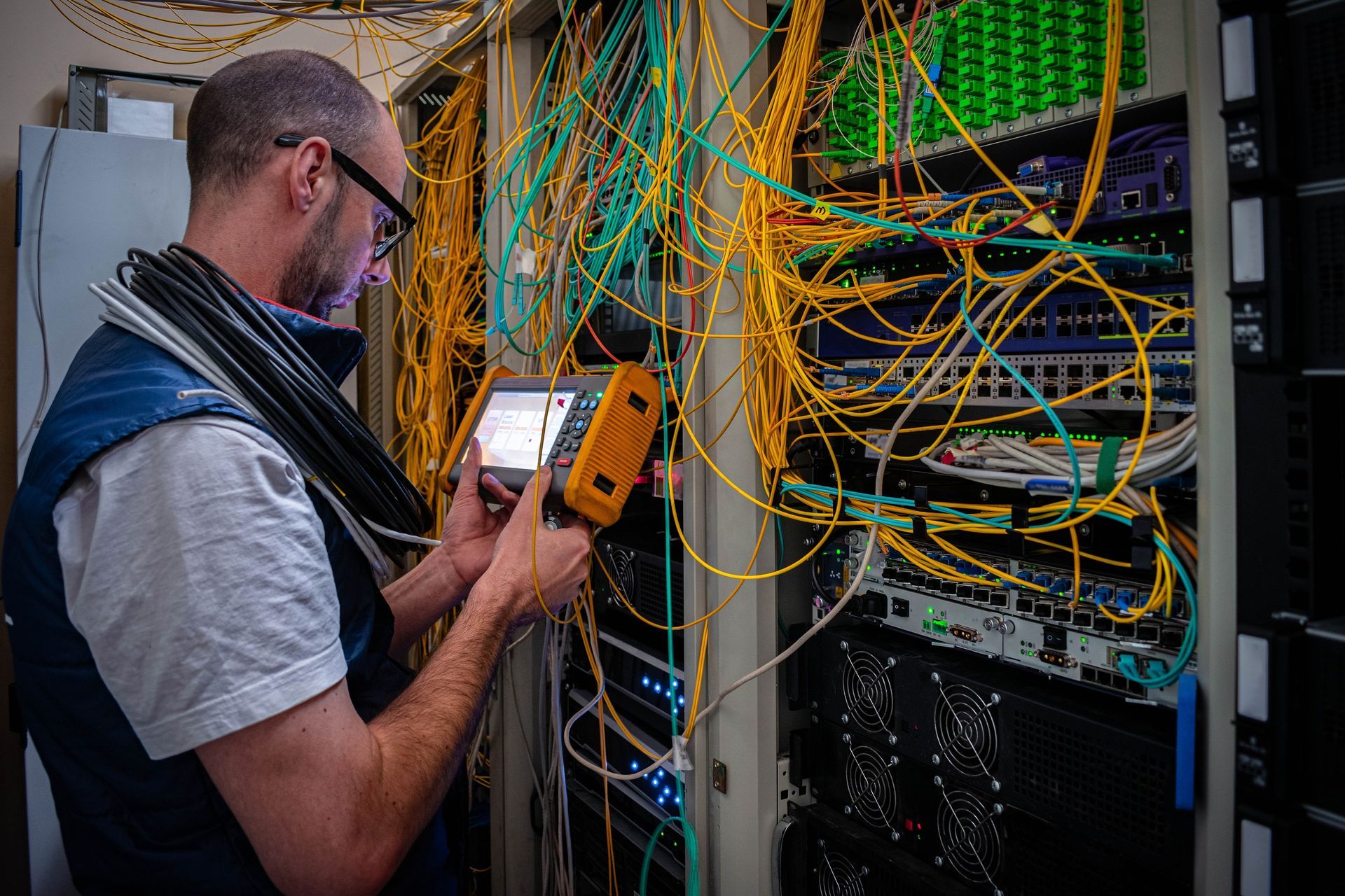 Man in Glasses Examines Server Rack, Tangled Cables, Holding Testing Device — SJD Electrical Contracting in Lithgow, NSW