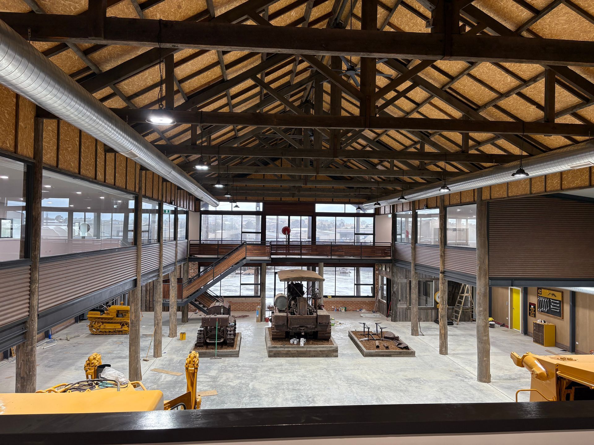Interior view of a museum with heavy machinery exhibits. Wooden beams and large windows.