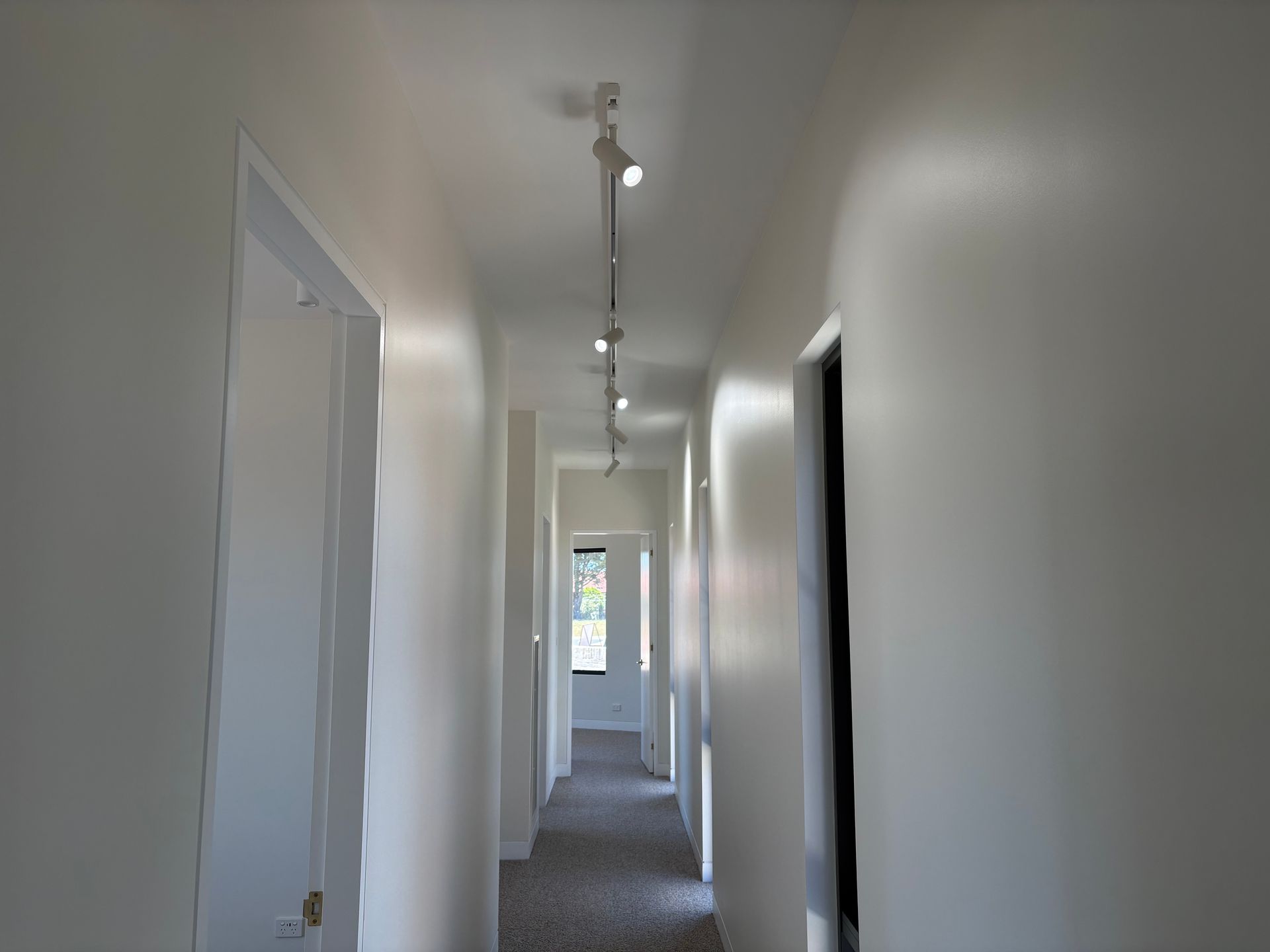 Long hallway with white walls and ceiling, doors, carpeted floor, and track lighting— SJD Electrical Contracting in Orange, NSW
