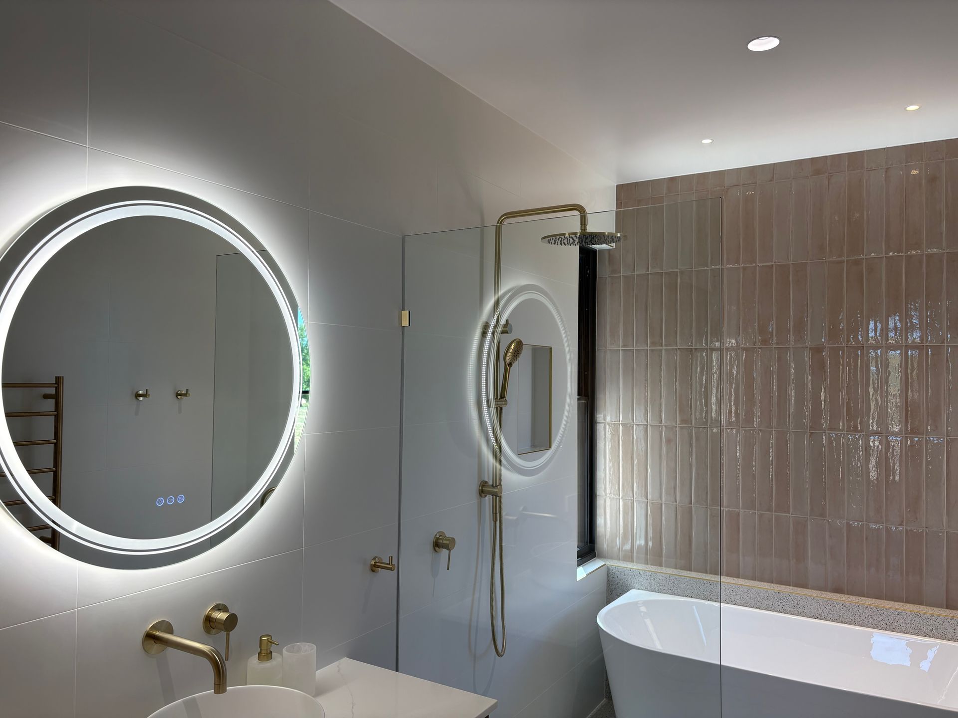 Modern bathroom with a round lighted mirror, gold fixtures, and a freestanding tub.