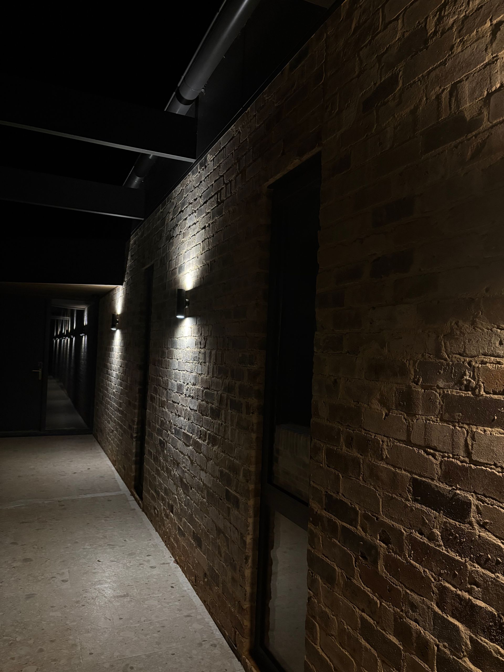 Brick hallway with sconce lighting, dark with a sense of depth.