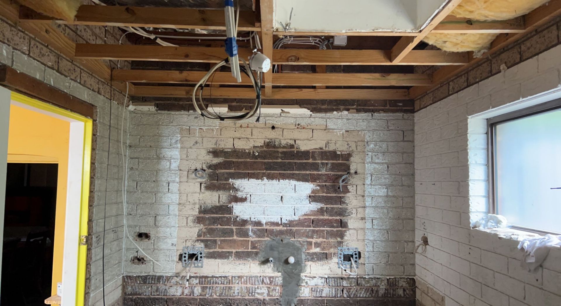 Bathroom under renovation; exposed brick wall, unfinished ceiling, window, water pipes, and electrical outlets— SJD Electrical Contracting in Orange, NSW