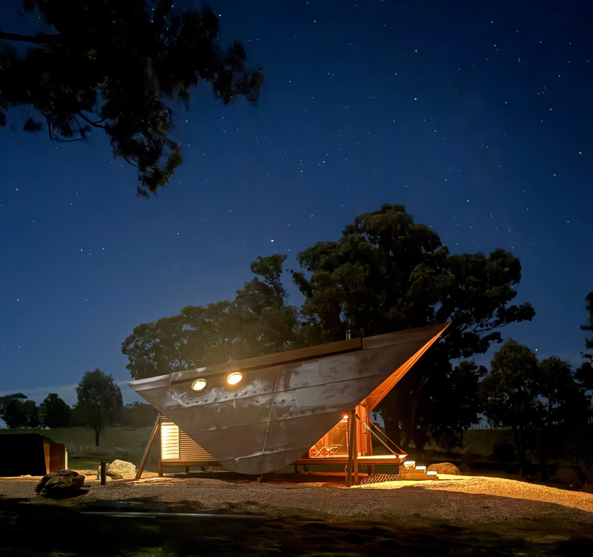 Quirky boat-shaped cabin at night under a starry sky, with warm interior lighting.