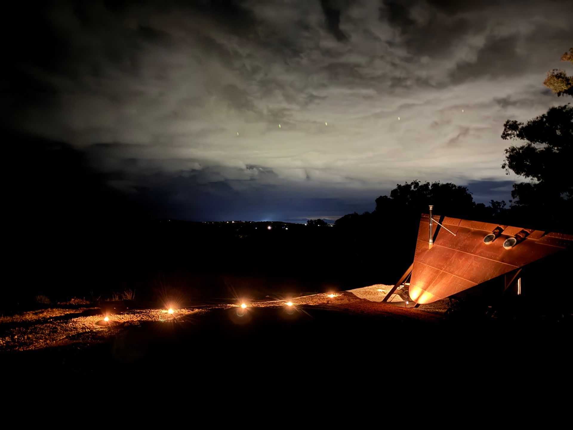 Night scene: lit ground with lights, dark silhouette, cloudy sky, small town lights.