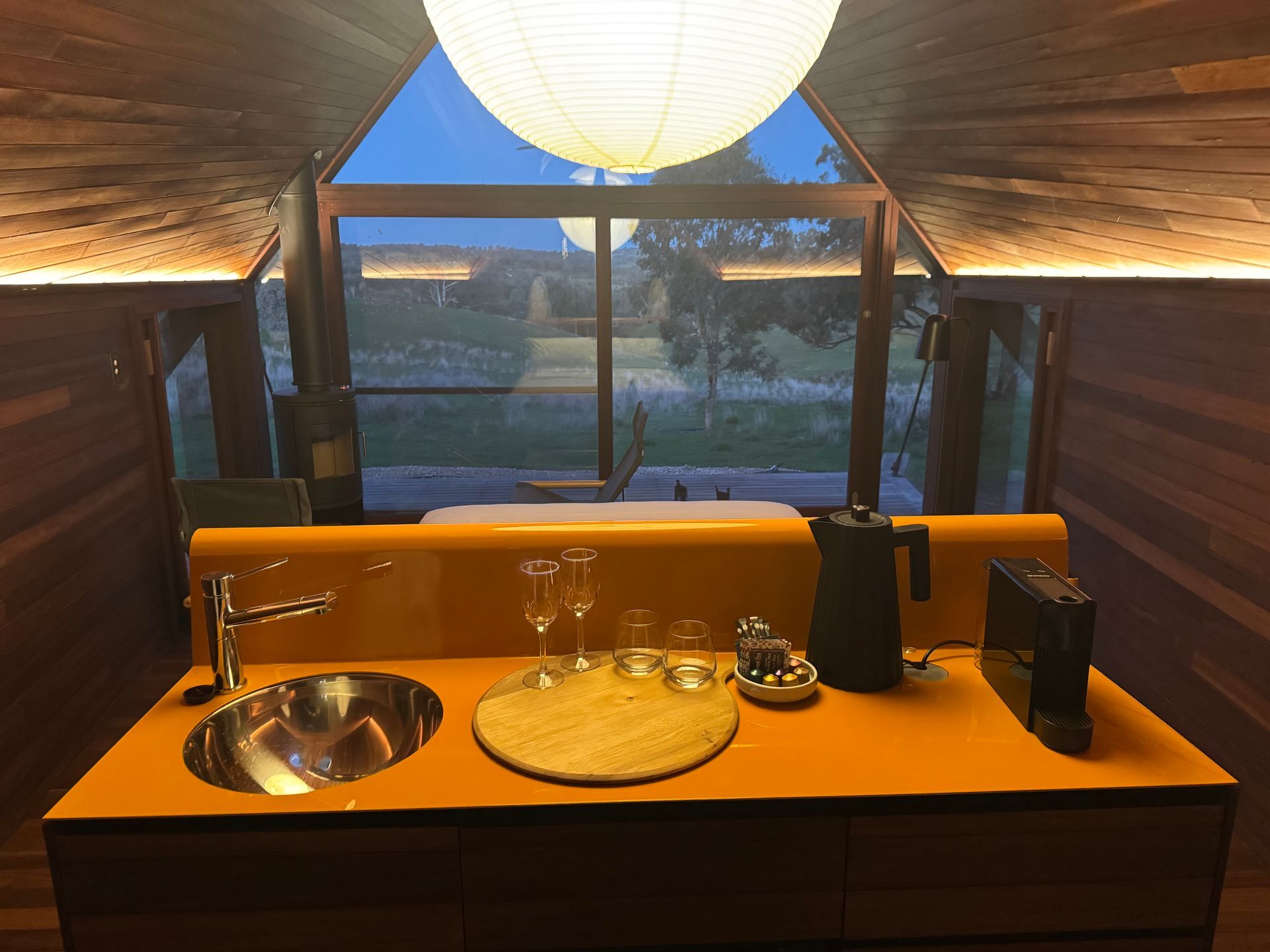 Interior of a wooden cabin with an orange countertop, sink, and kettle. Large window overlooks a landscape— SJD Electrical Contracting in Orange, NSW