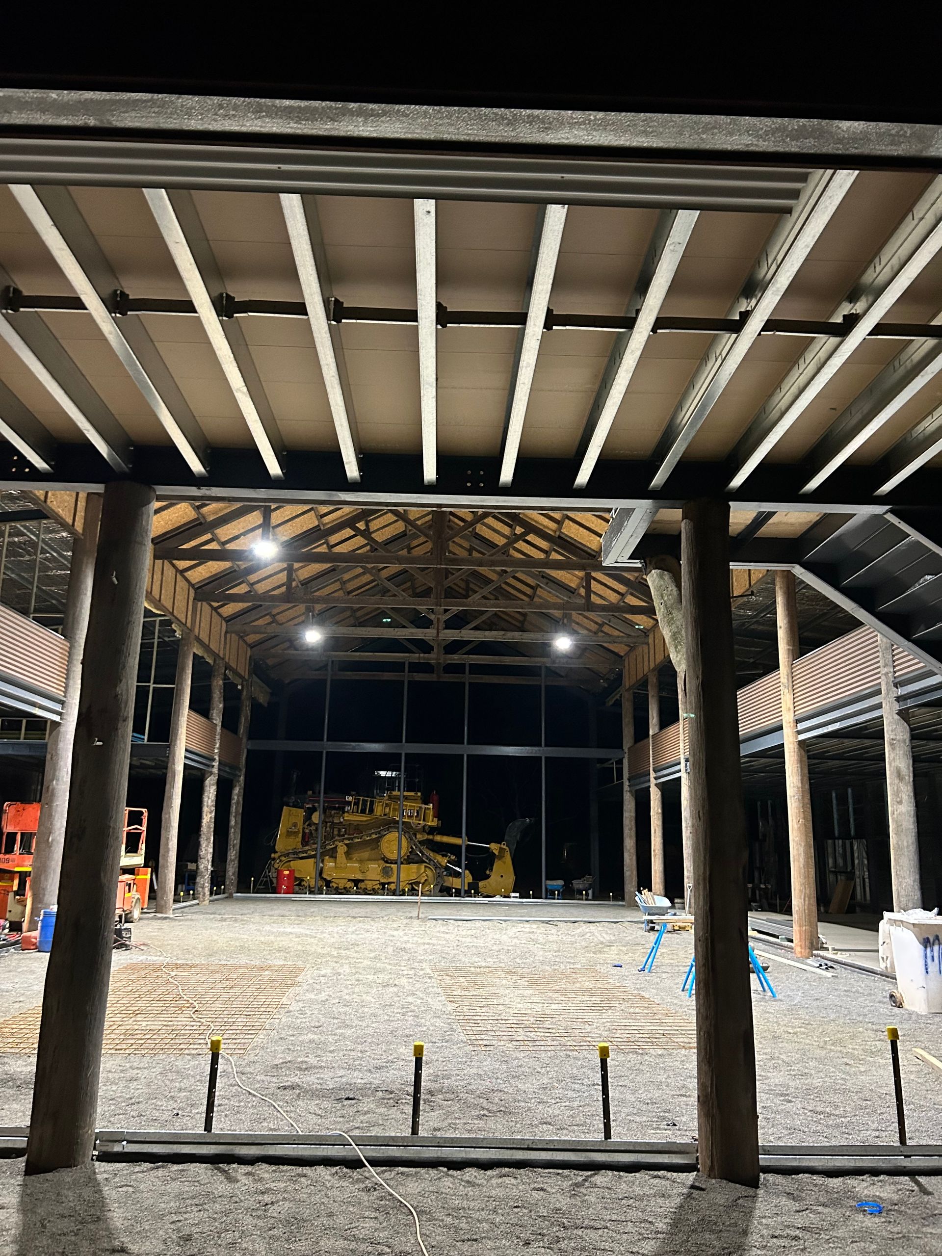 Inside a large, unfinished wooden structure at night; exposed beams, large windows, and construction equipment — SJD Electrical Contracting in Orange, NSW