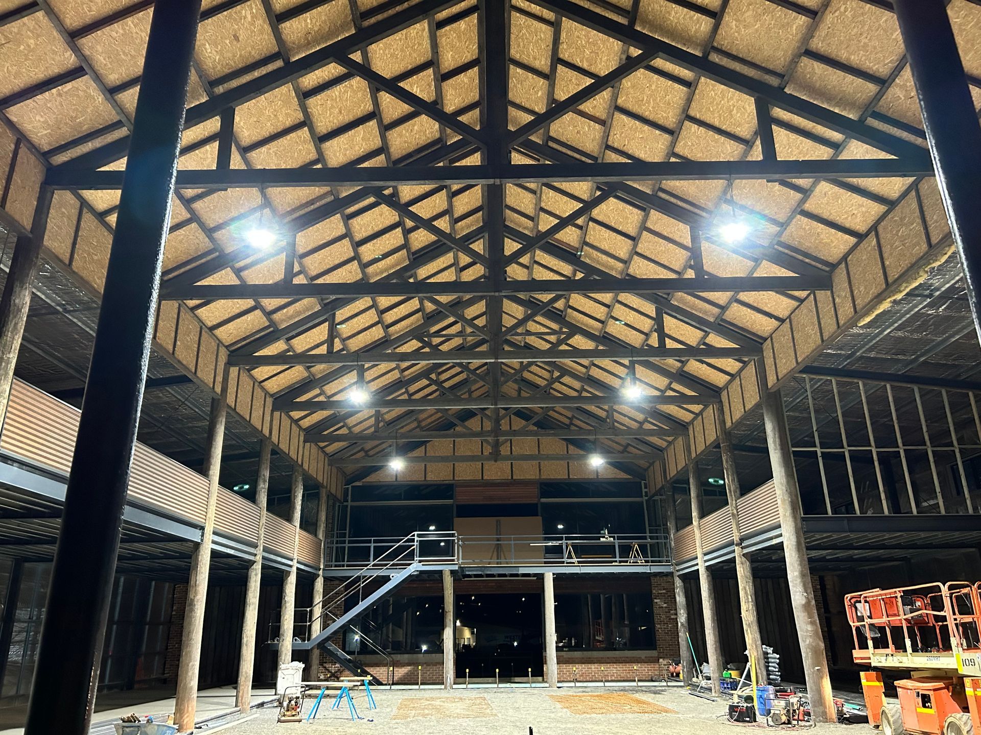 Interior of a large building with exposed wooden beams, a straw roof, and several bright lights.