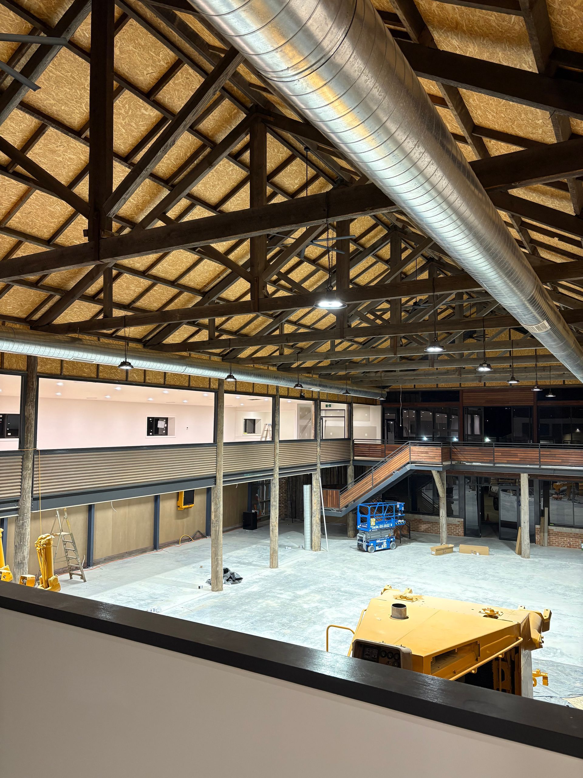 Large warehouse interior with wooden beams, gray floor, and construction equipment.