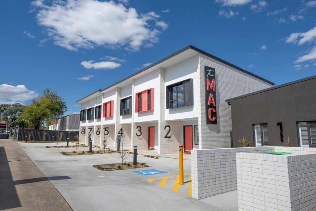 Motel exterior, white building with black and red accents, rooms numbered 2-5, blue sky.