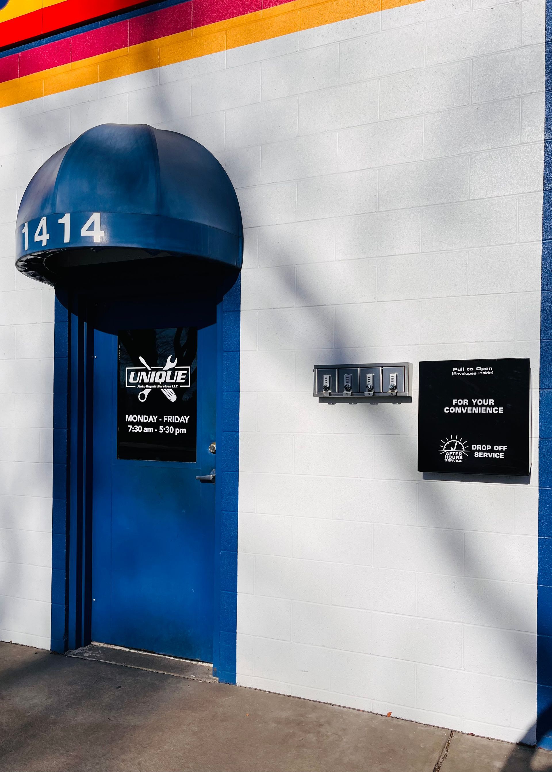 Blue door with awning, address 1414, sign, and mailbox on a white building exterior.