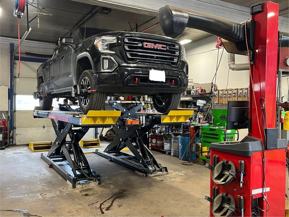 Black GMC truck raised on a scissor lift in a repair shop for wheel alignment.