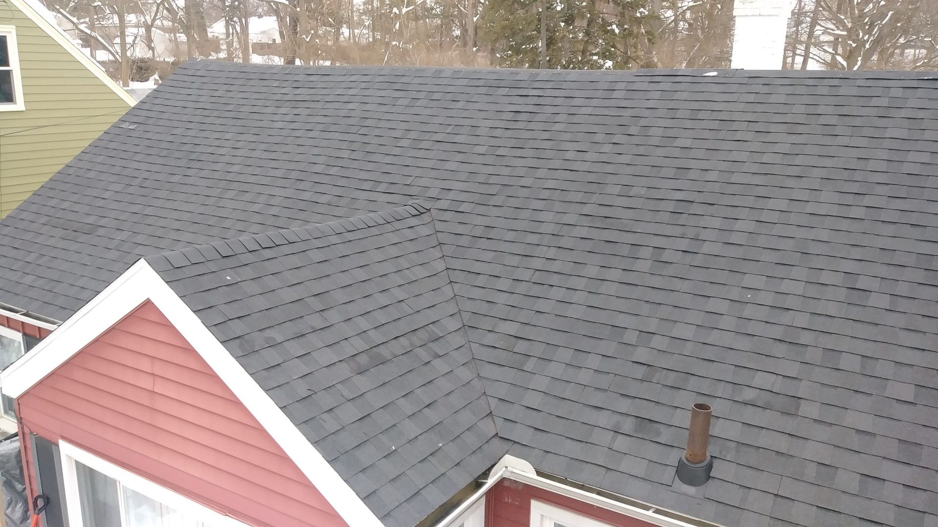 An elevated, angled view of a dark shingled roof on a house, featuring a small gabled section and a vent pipe.